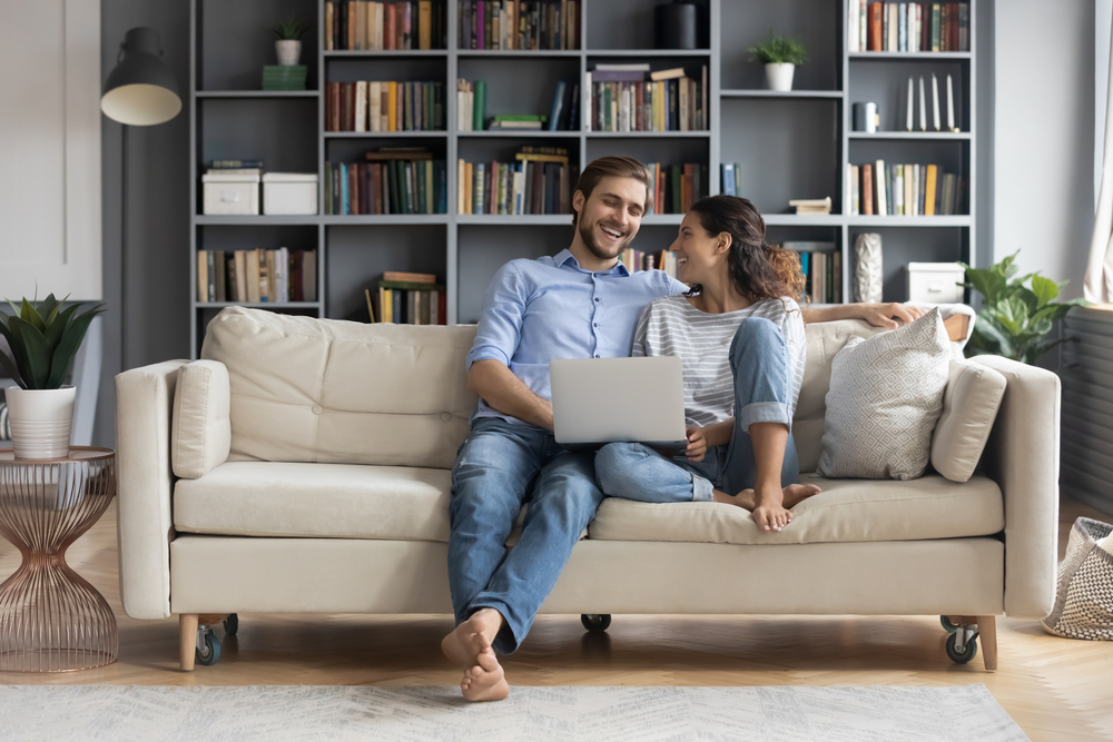 happy,young,relaxed,couple,sitting,on,sofa,with,laptop,on